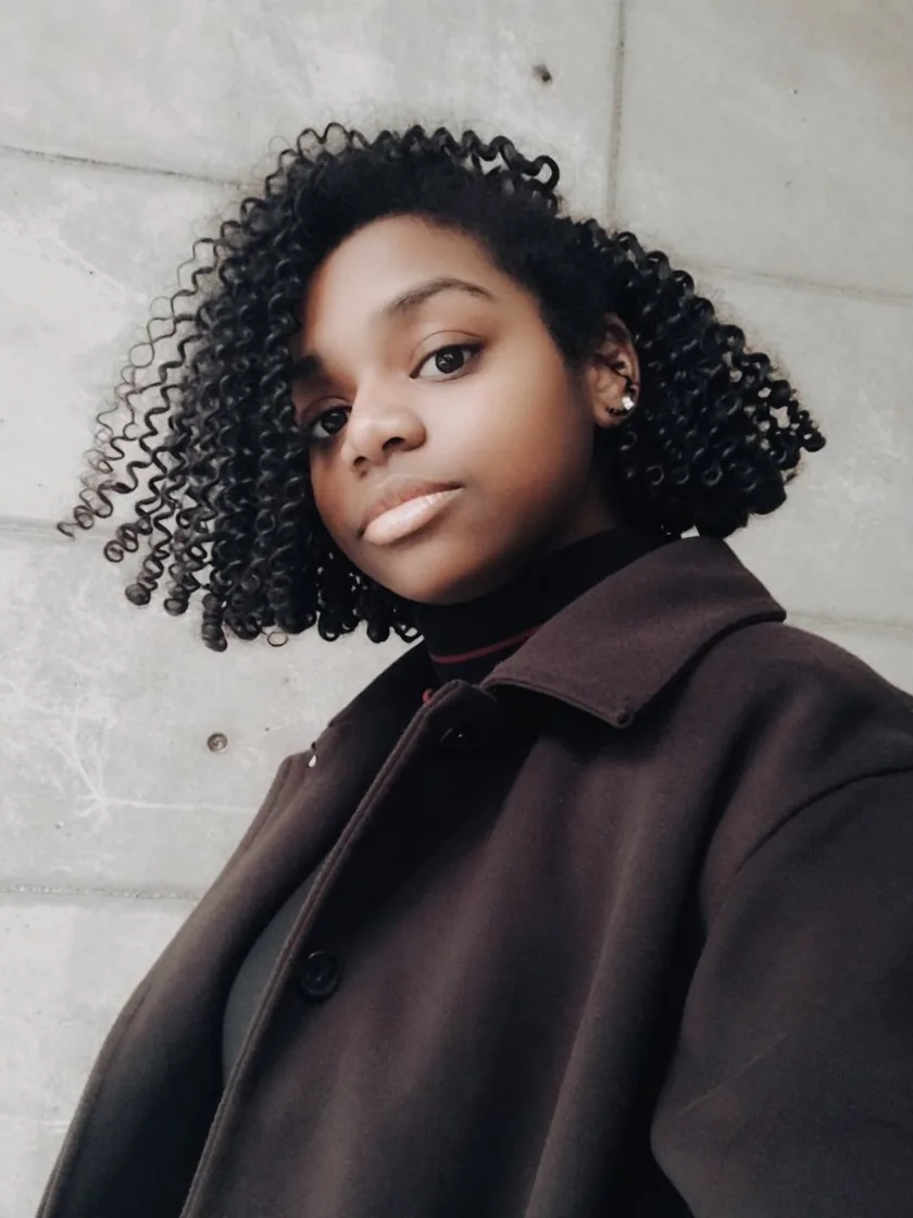 Angela Clemons, senior UX/UI designer, in a dark coat against a concrete wall